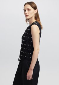 Top nero senza maniche con strisce orizzontali, decorato con borchie metalliche. Abbinato a pantaloni neri con cordoncino, caratterizzati da una vestibilità comoda.