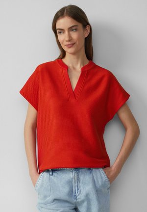 Haut rouge à manches courtes côtelé avec un décolleté en V, coupe décontractée et fentes sur les côtés, associé à un short en denim taille haute bleu clair.