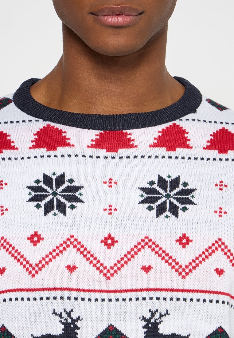 Sweter świąteczny dzianinowy w kolorze białym, z czerwonymi drzewkami, czarnymi płatkami śniegu i wzorami reniferów. Granatowy ściągacz przy okrągłym dekolcie i miękka faktura.