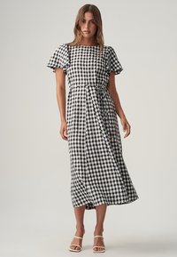 Black and white gingham maxi dress, short ruffled sleeves, cinched waist with ties, and a flowing skirt with a subtle sheen.