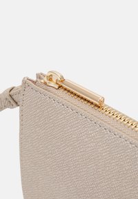 Texturovaná béžová kabelka s zlatým zipem a kováním. Detailní pohled zvýrazňuje zip a strukturu materiálu.