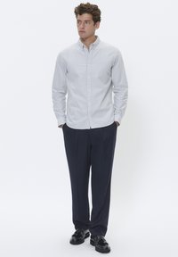 Gestreifte Button-Up-Bluse in Hellblau und Weiß, kombiniert mit dunklen Navy-Hosen. Die Bluse verfügt über einen klassischen Kragen und lange Ärmel.