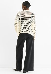 Cream open-knit sweater with wide sleeves, worn over dark wide-leg jeans. The sweater features a loose, airy texture and ribbed hem.