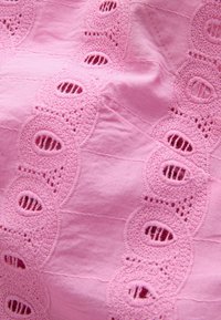 Tessuto rosa con ricami in occhio decorativi che presentano motivi circolari e ritagli, creando un aspetto leggero e testurizzato.