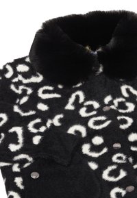 Svart och vit fuskpälsjacka med leopardmönster, rund svart krage och gråa knappar, med en mjuk, texturerad yta.