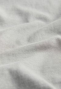 Lys grå stof med en glat, let struktureret overflade. Stoffet ser blødt ud og falder blidt, hvilket afslører fine, subtile linjer.