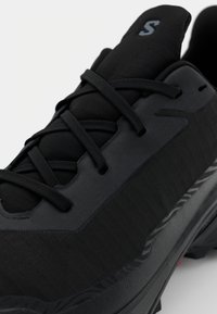 Sneaker noire avec une tige texturée, un système de laçage et une semelle en caoutchouc avec un motif de semelle. Les accents incluent un logo discret sur la languette.