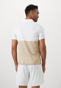 Kortærmet polo-shirt med hvid øverste del og beige nederste del. Fremstillet af et glat stof, med en klassisk krave og en afslappet pasform.
