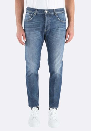 Jeans in denim azzurro chiaro con vestibilità slim, cinque tasche e cuciture a contrasto, abbinati a sneakers bianche.