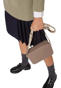 Borsa a tracolla rettangolare marrone con finitura testurizzata e una tracolla decorata. Indossata con una gonna scura a pieghe e scarpe nere. Calzini grigi a coste visibili.