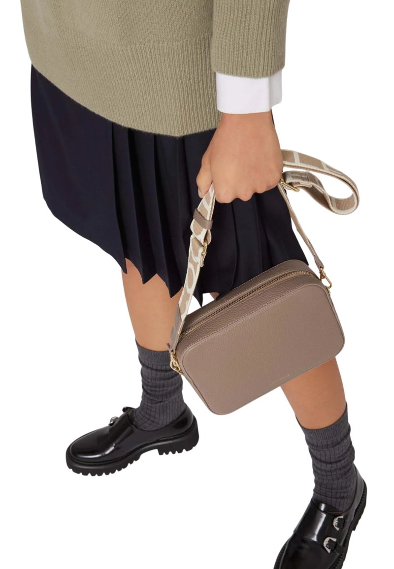 Borsa a tracolla rettangolare marrone con finitura testurizzata e una tracolla decorata. Indossata con una gonna scura a pieghe e scarpe nere. Calzini grigi a coste visibili.