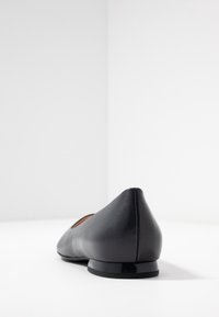 Black leather ballet flat with a pointed toe, low heel, and smooth texture. Minimalist design with a subtle finish.