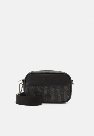 Sac bandoulière noir texturé avec un motif géométrique, fermeture éclair et bandoulière ajustable ; agrémenté d'un logo Lacoste.