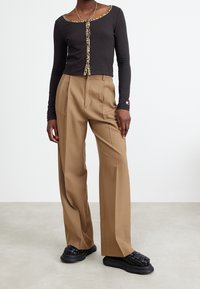 Svart långärmad topp med leopardmönstrad kant och knappar, tillsammans med vida beige byxor och svarta vävda slip-on skor.