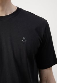 Zwart katoenen T-shirt met een ronde hals, korte mouwen, met een klein wit "M OP" logo op de borst. Gladde textuur en een comfortabele pasvorm.