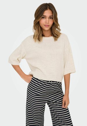 Pull en tricot côtelé crème à manches courtes et col rond, associé à un pantalon large rayé bleu marine et blanc avec une taille élastique.