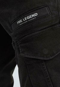 Schwarze Cargo-Hosen aus strukturiertem Stoff mit einer Seitentasche und einem Etikett, auf dem "PME Legend American Classic" aufgestickt ist.