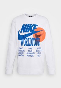 Pitkähihaisessa valkoisessa hupparissa on sininen "NIKE" -teksti, "WORLDTOUR" -merkintä ja siniset kaupunkien nimien painatukset, sekä punainen ympyräkoriste.