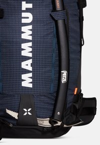 Mammut ryggsekk i marineblå med rutemønster, utstyrt med en svart stropp, utstyrsløkker og en sølvkarabin. Holdbart materiale og funksjonelt design.