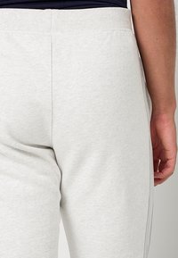 Hellgraue Jogginghose aus strukturiertem Stoff. Mit tailliertem Bund und Seitennähten. Die Rückansicht zeigt glatte Konturen ohne Verzierungen.