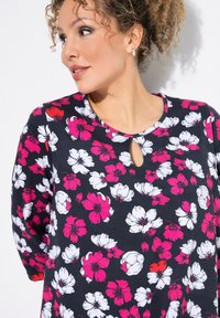 Bloementunika in marineblauwe stof, met witte en roze bloemen, ronde halslijn met een sleutelgat uitsnijding en driekwart mouwen.