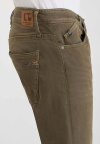Pantalons vert olive en tissu durable, avec plusieurs poches, des coutures visibles et une étiquette en cuir au-dessus de la poche arrière.