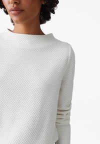 Witte gebreide trui met een ronde halslijn en gathered mouwen. Gemaakt van geweven stof, met een subtiel patroon voor extra detail.