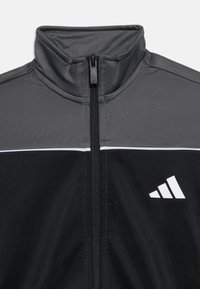 Μαύρο και γκρι αθλητικό μπουφάν με φερμουάρ μπροστά και λευκό λογότυπο Adidas στη δεξιά πλευρά του στήθους, με ψηλό γιακά.