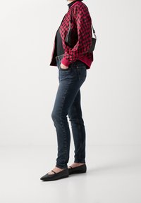 Red and black checkered bomber jacket, black top, dark blue skinny jeans, and black flats with cutout accents. Simple look with modern lines.