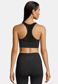 Svart sports-bh med mesh-bakdesign. Toppen har en racerback-form. Kombinert med høyt midjebånd svarte tights med tekstdetaljer.