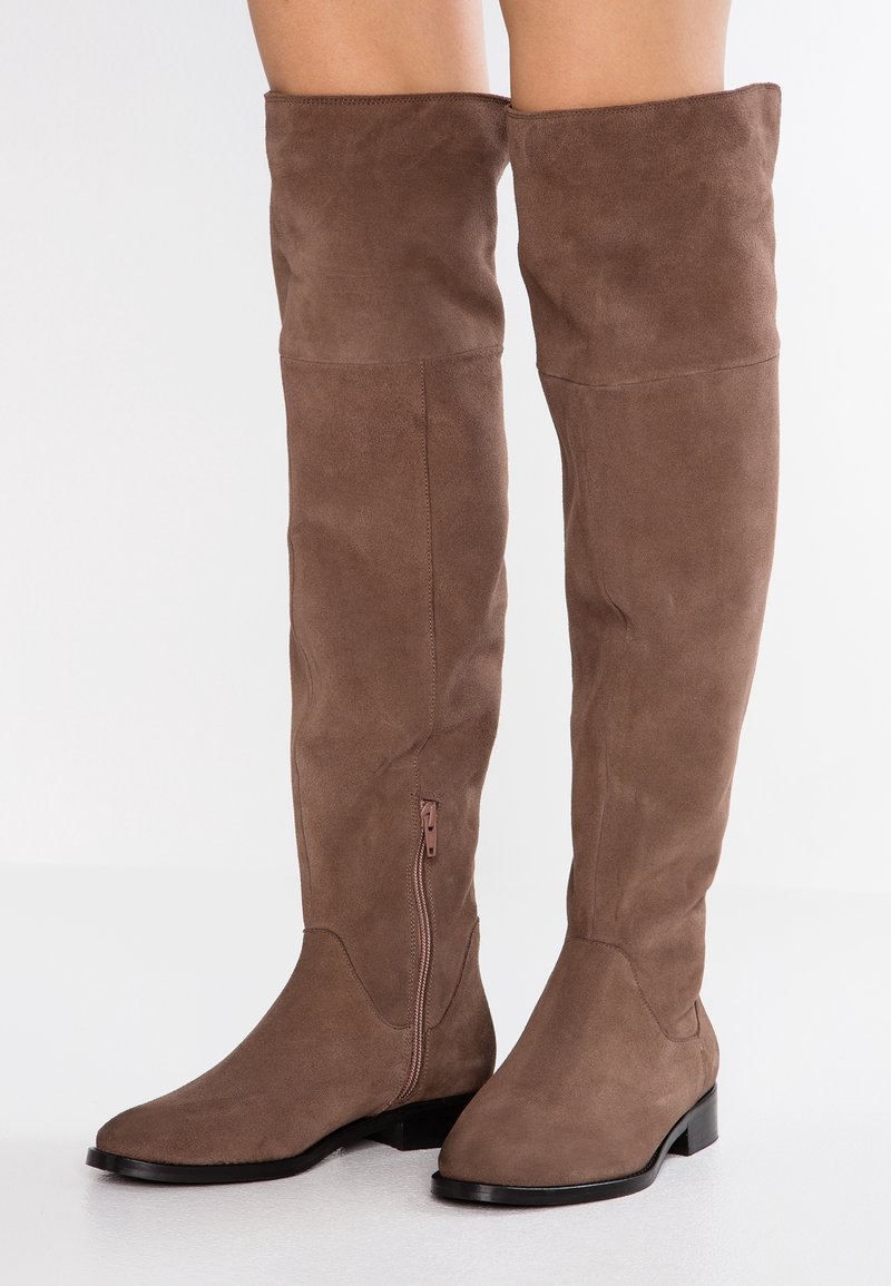 Brązowe zamszowe kozaki za kolano z płaskim obcasem i bocznym zamkiem. Miękka tekstura, bezszwowy design i zaokrąglony kształt czubka.