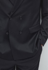 Giacca da tale nero doppiopetto con tessuto testurizzato, due tasche frontali e due bottoni neri con finitura liscia. Design aderente.