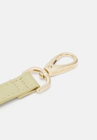 Guldmetallspänne fäst vid ett ljusgrönt läderrem, med stygndetaljer och ingraverat varumärkesnamn.