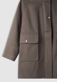 Cappotto marrone, textured con due tasche frontali, chiusure a scatto e una vestibilità rilassata. Presenta dettagli di cucitura sottili e maniche ampie.