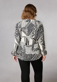 Blusa a maniche lunghe con un motivo geometrico in bianco e nero, caratterizzata da varie forme e textures, abbinata a leggings neri.