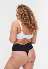 Reggiseno bianco con spalline regolabili e chiusura a gancio, abbinato a culotte nere a vita alta. Tessuto liscio con cuciture minime.