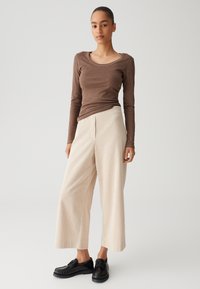 Brown long-sleeve top with scoop neck, paired with cream wide-leg ribbed pants and black lace-up shoes. Simple and textured design.