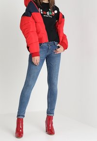 Červená prošívaná bunda s námořnicky modrými doplňky, černé tričko s potiskem, modré úzké džíny a lesklé červené boty na vysokém podpatku.