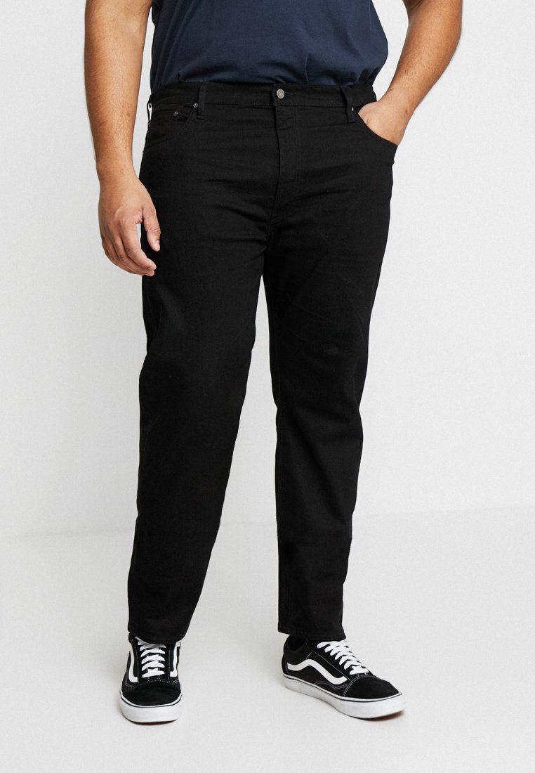 Jeans de mezclilla negra con corte recto, que cuentan con un diseño clásico de cinco bolsillos y detalles de costura sutiles; combinados con zapatillas negras y blancas.