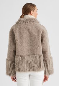 Beige Kunstfelljacke mit flauschigem Pelzbesatz an den Ärmelbündchen und am Saum. Sie hat eine weiche Textur und ein lässiges Design mit einem breiten Kragen.