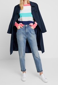 Marinblå trenchcoat över en randig tröja i blått, rosa och grått. Ljusblå högmidjade jeans och vita sneakers fulländar looken.