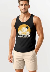 Schwarzes Tanktop mit einem gelben, runden Grafikdesign von Palmen und dem Text "CALIFORNIA SOUTH BEACH." Getragen mit cremefarbenen Shorts.