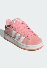 Pink suede sneaker with white leather stripes, round logo on tongue, textured laces, and a rubber sole featuring a light brown accent.