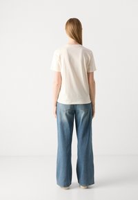 T-shirt in cotone crema abbinato a jeans a gamba larga blu chiaro. La maglietta presenta un taglio classico con un colletto semplice e maniche corte.