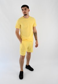 Conjunto de camiseta y pantalones cortos de algodón amarillos con cuello redondo y bolsillos laterales. Combinado con zapatillas deportivas negras. Diseño simple y casual.