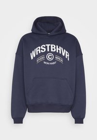 Sudadera azul marino con un bolsillo tipo canguro, puños y dobladillo acanalados. Presenta texto blanco: "WRSTBHVR STUDIO BERLIN MON HABIT" en un diseño curvado.