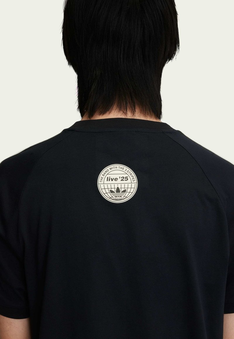 T-shirt nero con una patch rotonda sul retro alto, con testo ed elementi di design in colore chiaro contro il tessuto scuro.