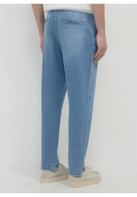 Jean en denim bleu clair avec une coupe décontractée, doté d'une poche arrière et d'une finition unie. Porté avec des baskets gris clair.