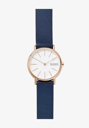 Reloj Skagen con caja dorada rosa, esfera blanca y correa de cuero azul marino. Presenta un diseño minimalista con marcadores de hora delgados y manecillas.