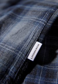 Blauw geruit stof met een gem textured afwerking, voorzien van een wit label dat met "LINDBERGH" aan de rand is gestikt.